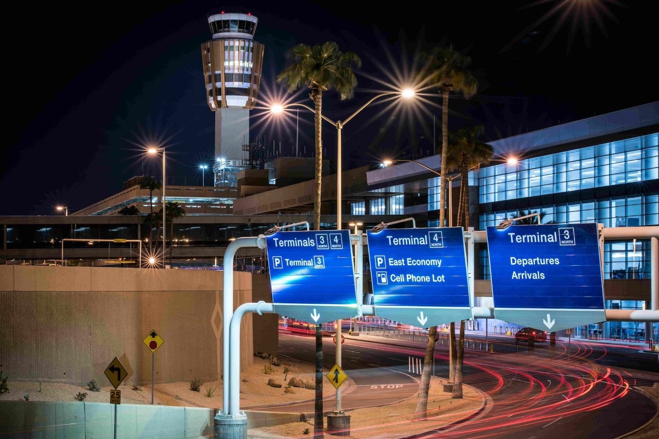 Phoenix Sky Harbor airport at night. Highway signs show directions to various terminals, and red lights indicate traffic moving at high speed.