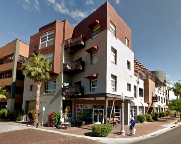 Three-story apartment building surrounded with a business on the ground floor, and ample sidewalks.
