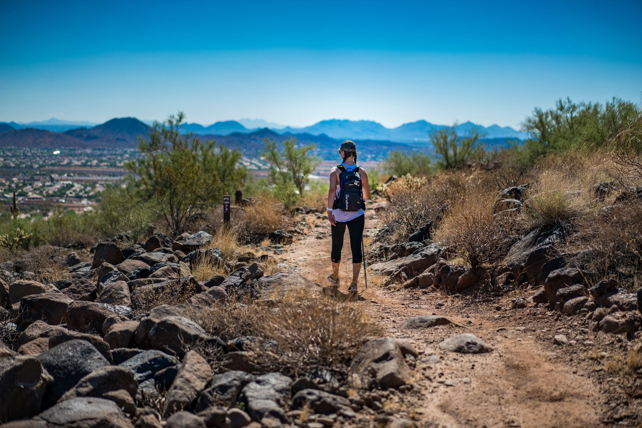 A lone hiker stands on a trail and looks at distant mountains.
